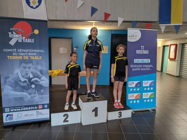 Les trois jeunes joueuses sur le podium, devant les bannières du Comité du Haut-Rhin et de la FFTT